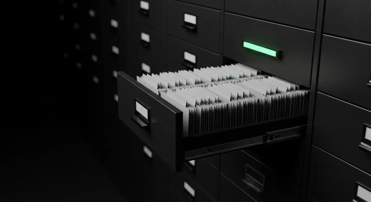 An archive card index in a dark room with one drawer pulled open and a green indicator lamp above it.